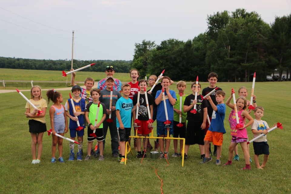 A group of kids holding model rockets around the launch pad.